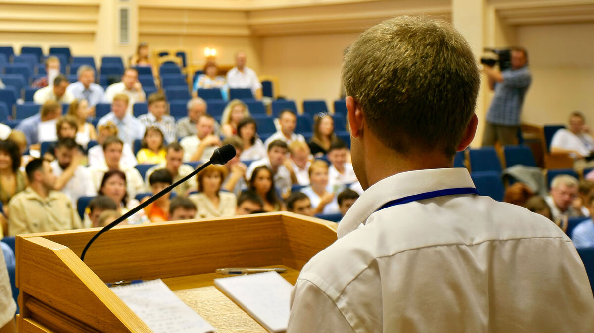 The Next Generation A person speaking at a University Assembly from the podium to a large group of people
